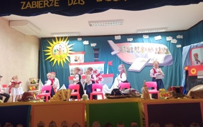 Dzień Babci i Dziadka. Na scenie pięć dziewczynek ubranych w regionalne sukienki tańczy z gazetami wokół krzeseł. Z tyłu gruzińska flaga. W tle kotara z samolotem i statkiem z wizerunkami dzieci. Z przodu sceny papierowy pociąg z wizerunkami dzieci.
