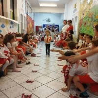 Pokaz Mody Patriotycznej. Chłopiec w białej koszuli, czerwonym krawacie, kokardzie narodowej oraz w ręku z flagą idzie korytarzem przedszkola. W tle tablica z napisem: Pokaz Mody Patriotycznej.