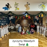 Wesołych Świąt. Dzieci występujące podczas jasełek w strojach pozują do zdjęcia. Za nimi trzy panie. Na dole zdjęcia napis: 